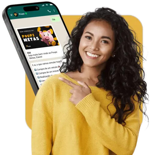 Mulher parda, cabelo preto, ondulado e solto, usando blusa amarela de manga longa, sorrindo e apontando para um Qr code posicionado ao lado dela. Ao fundo, um celular com tela de uma conversa no aplicativo WhatsApp.